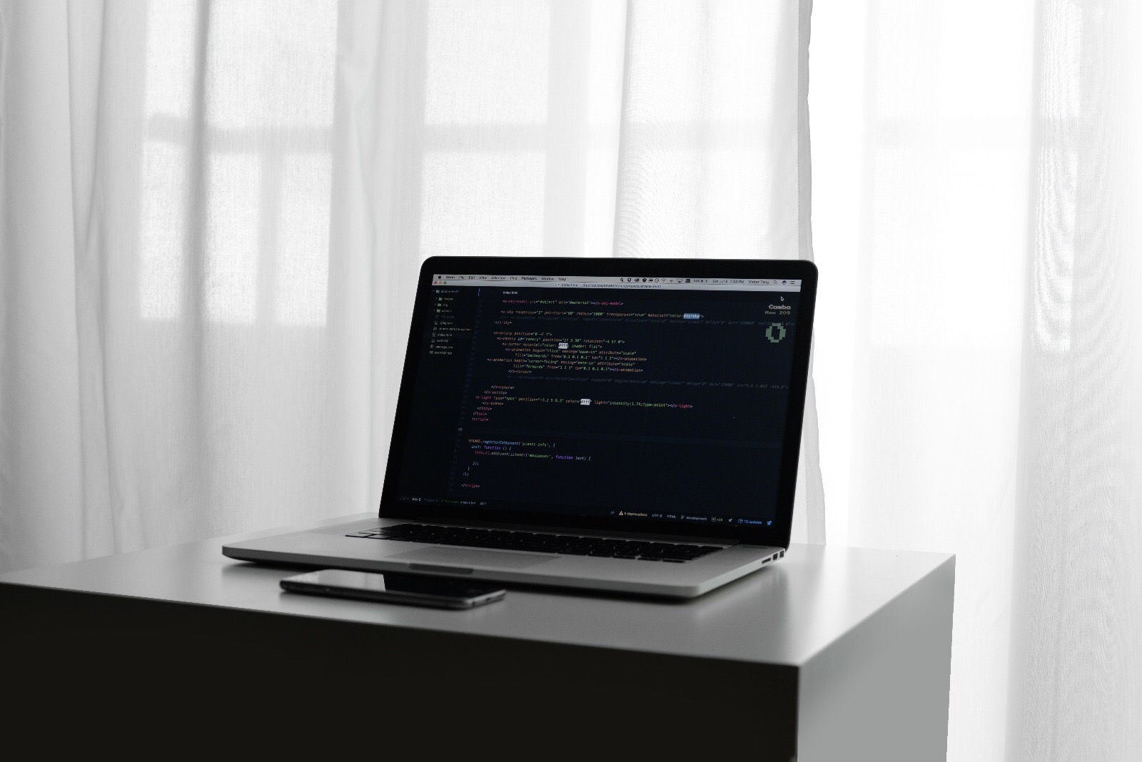 Laptop open to code on a desk in front of a sunlit curtain